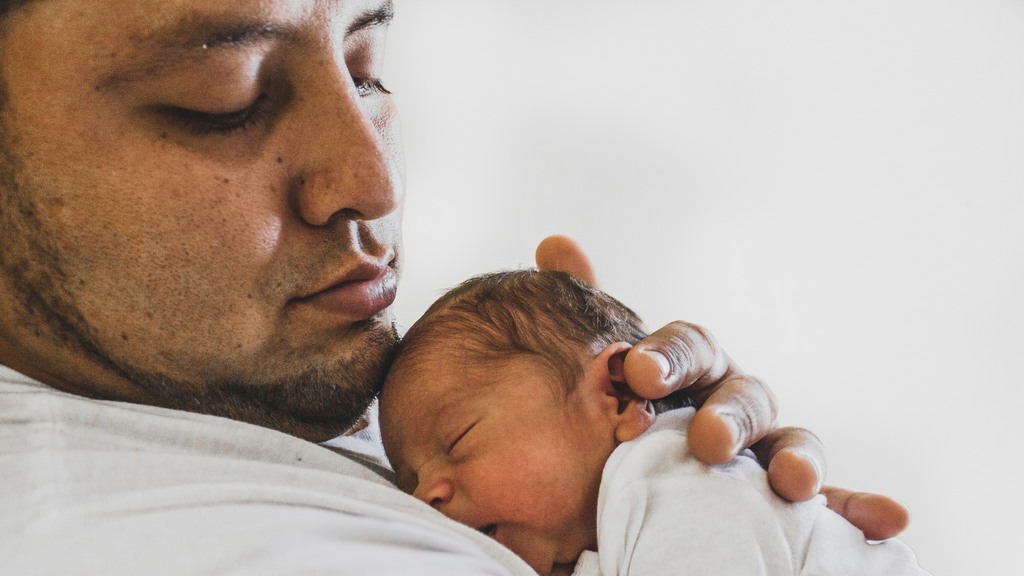 New father cradling newborn baby to chest.