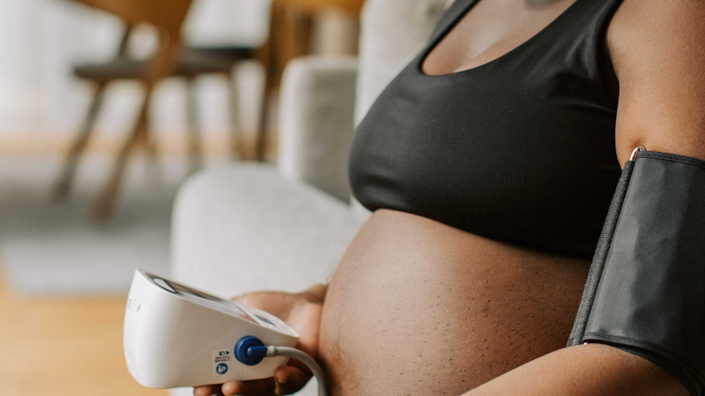 Pregnant black woman holding out her arm and wearing a pressure cuff to measure her blood pressure.